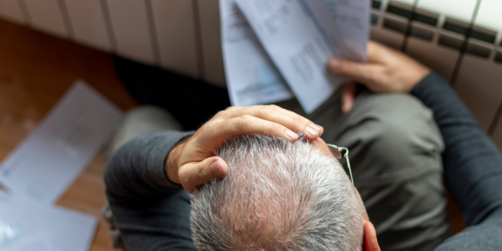 hombre adulto mayor preocupado sujeta su cabeza con una mano y tiene cuentas en la otra mano