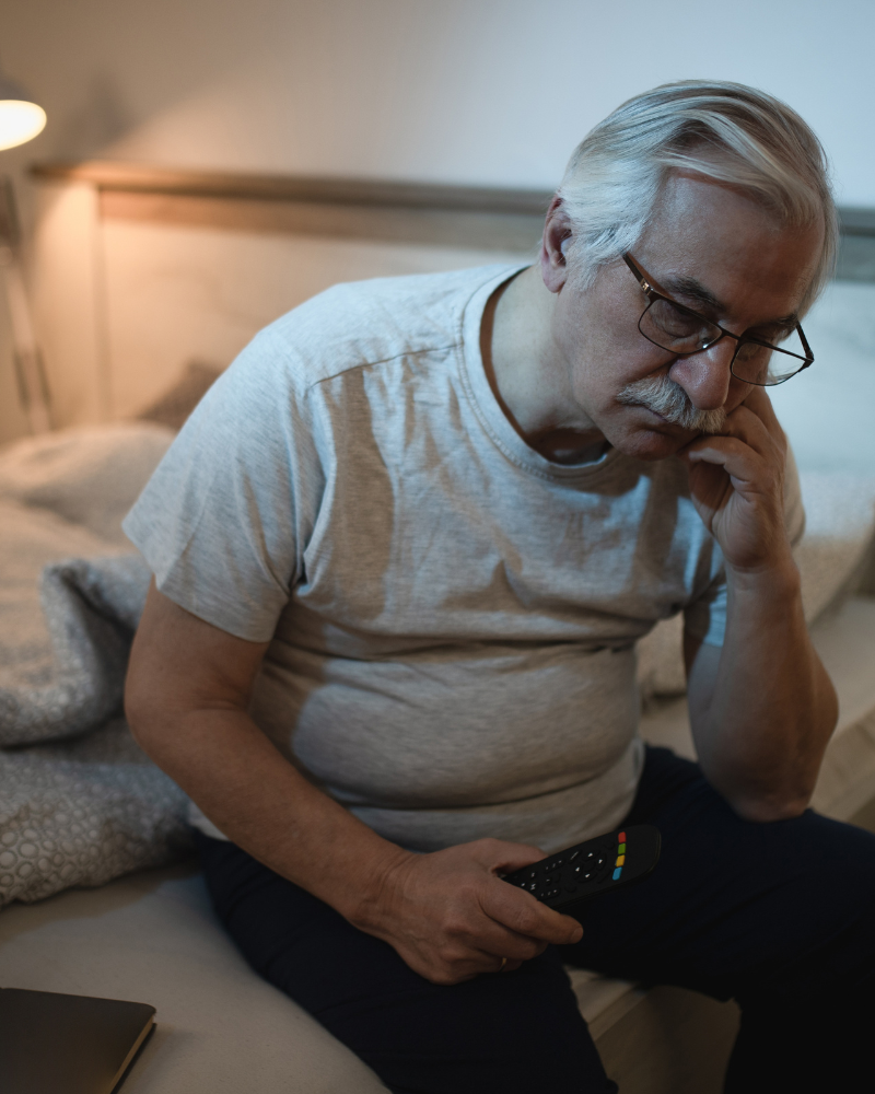 hombre adulto mayor sentado en pijama al borde de la cama con insomnio