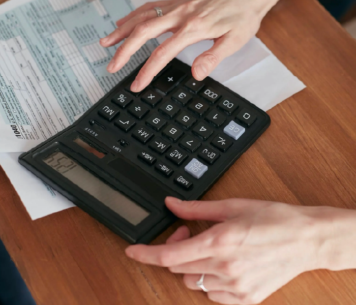 Manos sacando cuentas con calculadora y boletas sobre la messa